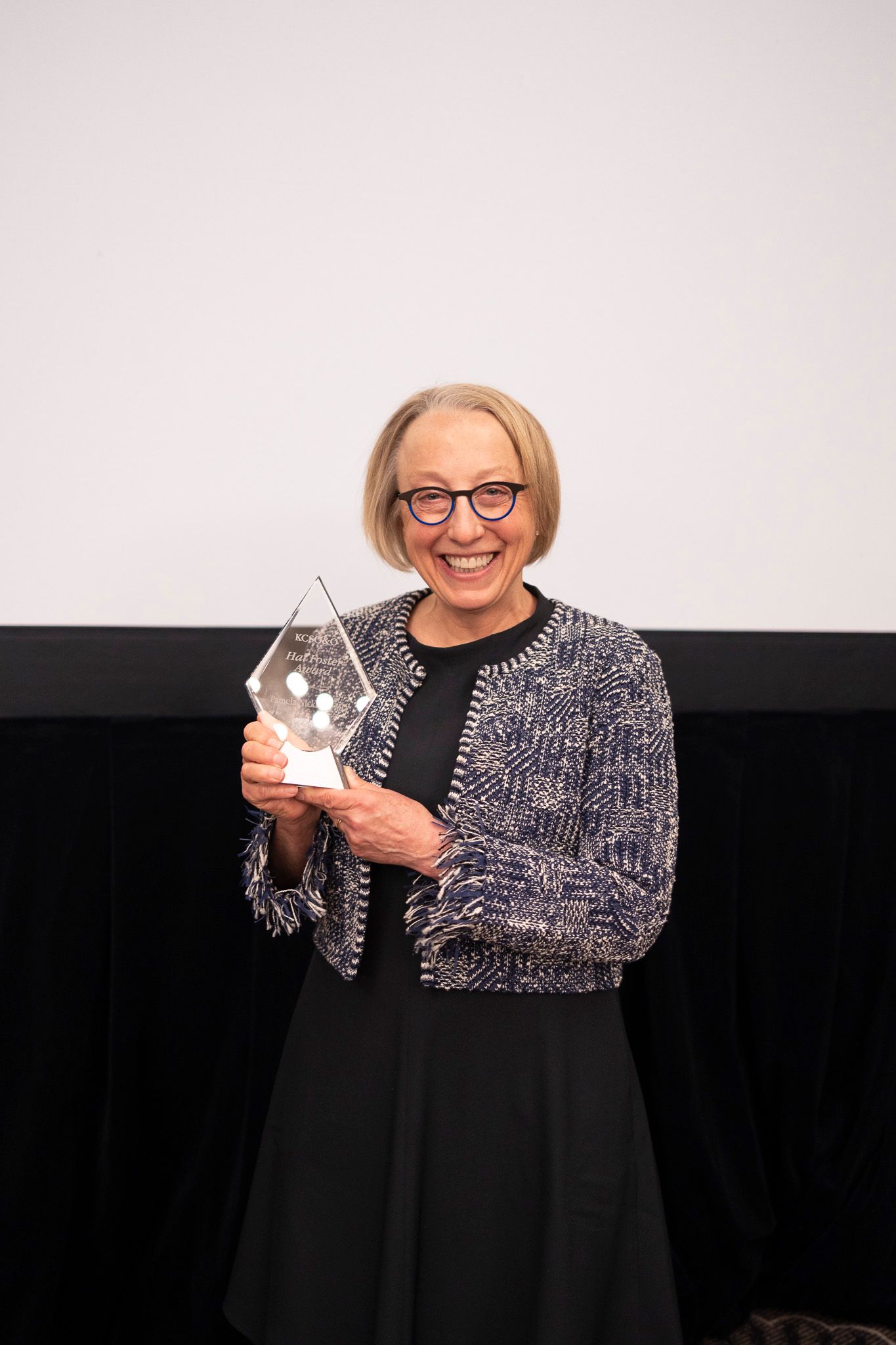 A woman is holding a trophy in front of a screen.