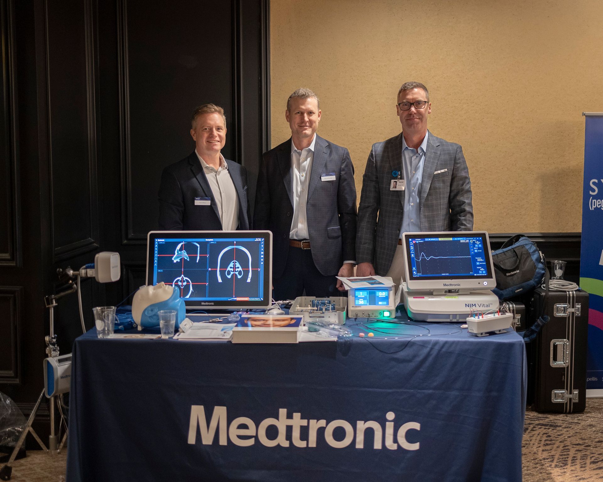 Three men are standing around a table with a medtronic sign on it.