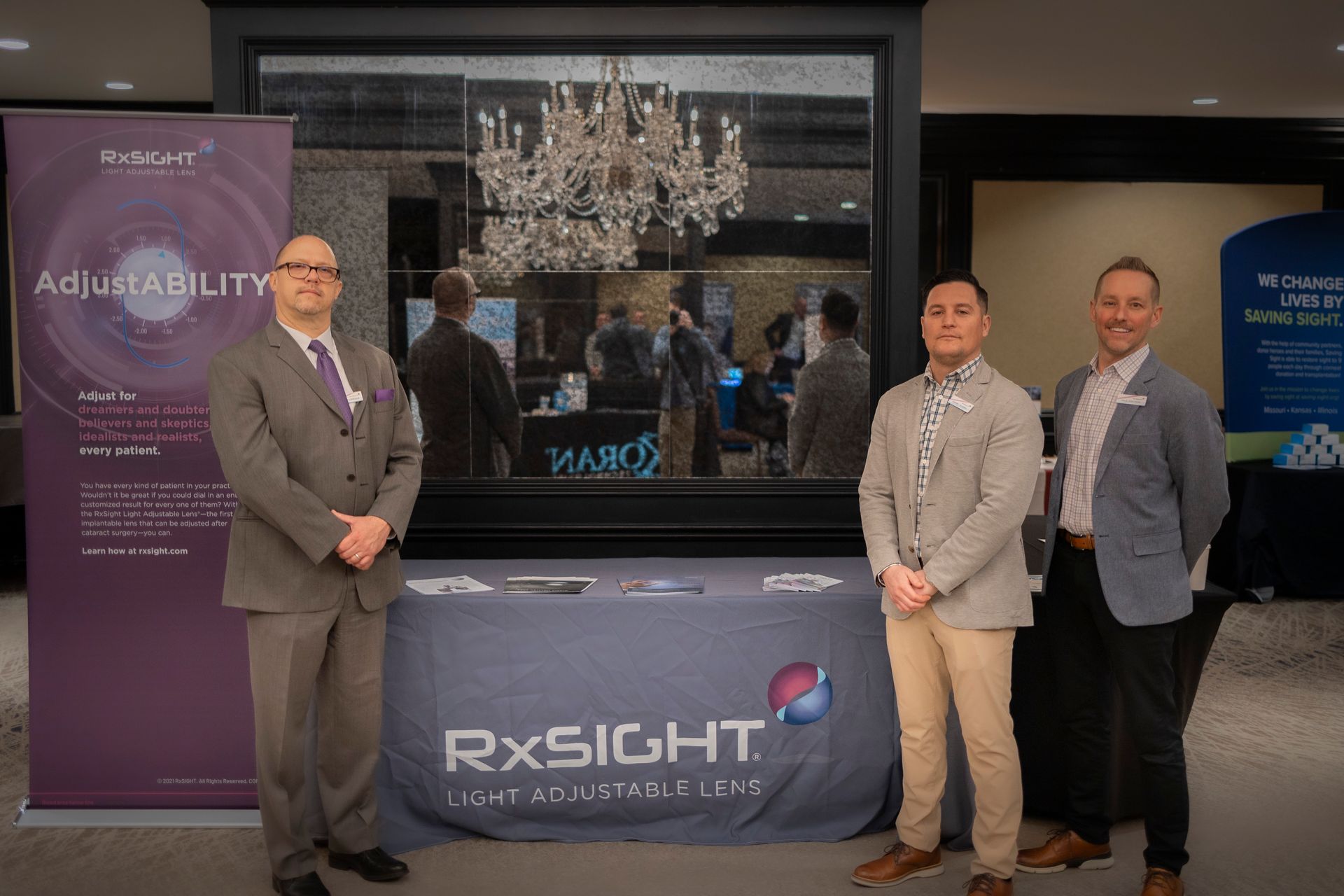 Three men are standing in front of a table with a sign that says rxsight.