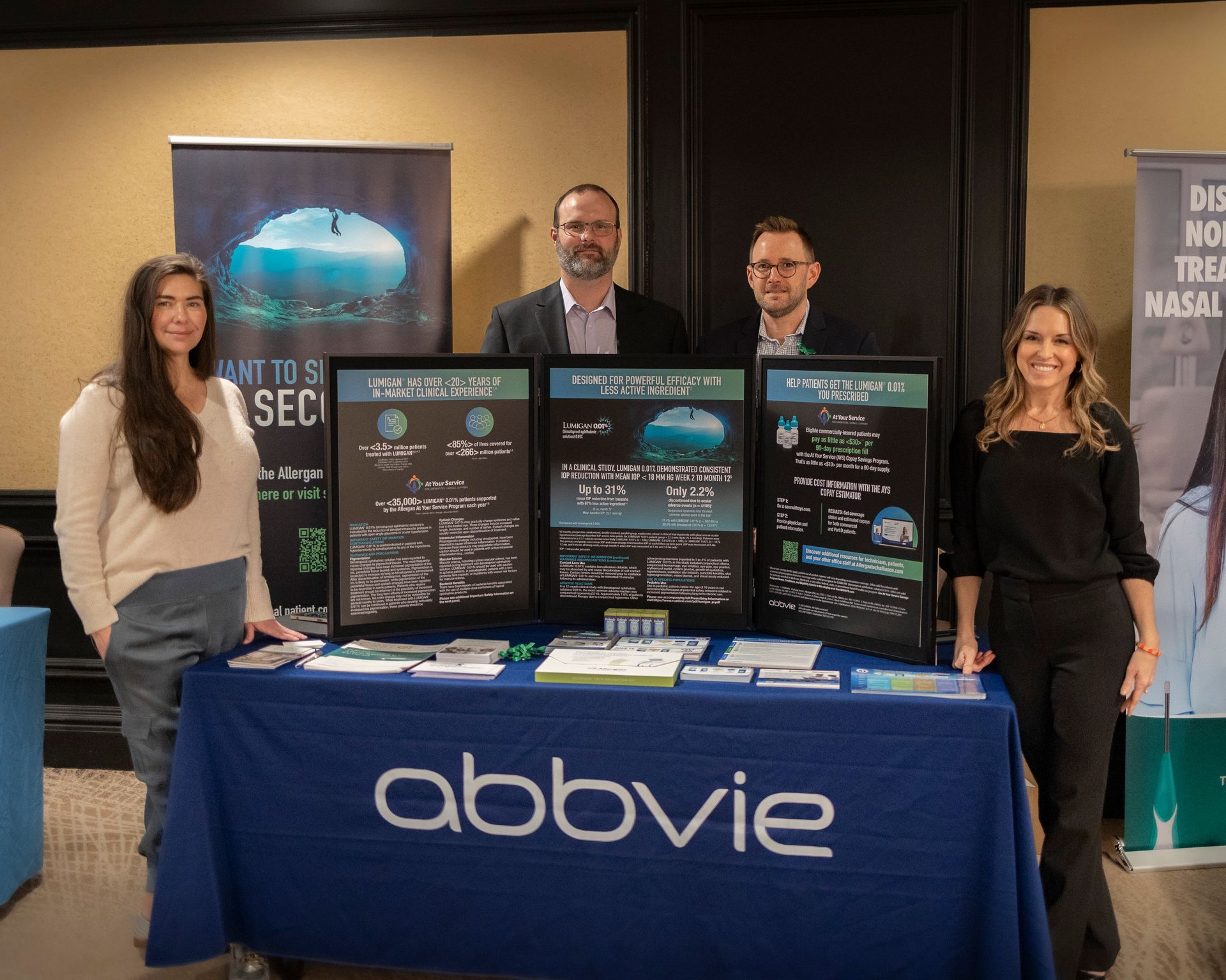 A group of people are standing around a table that says abbvie on it.