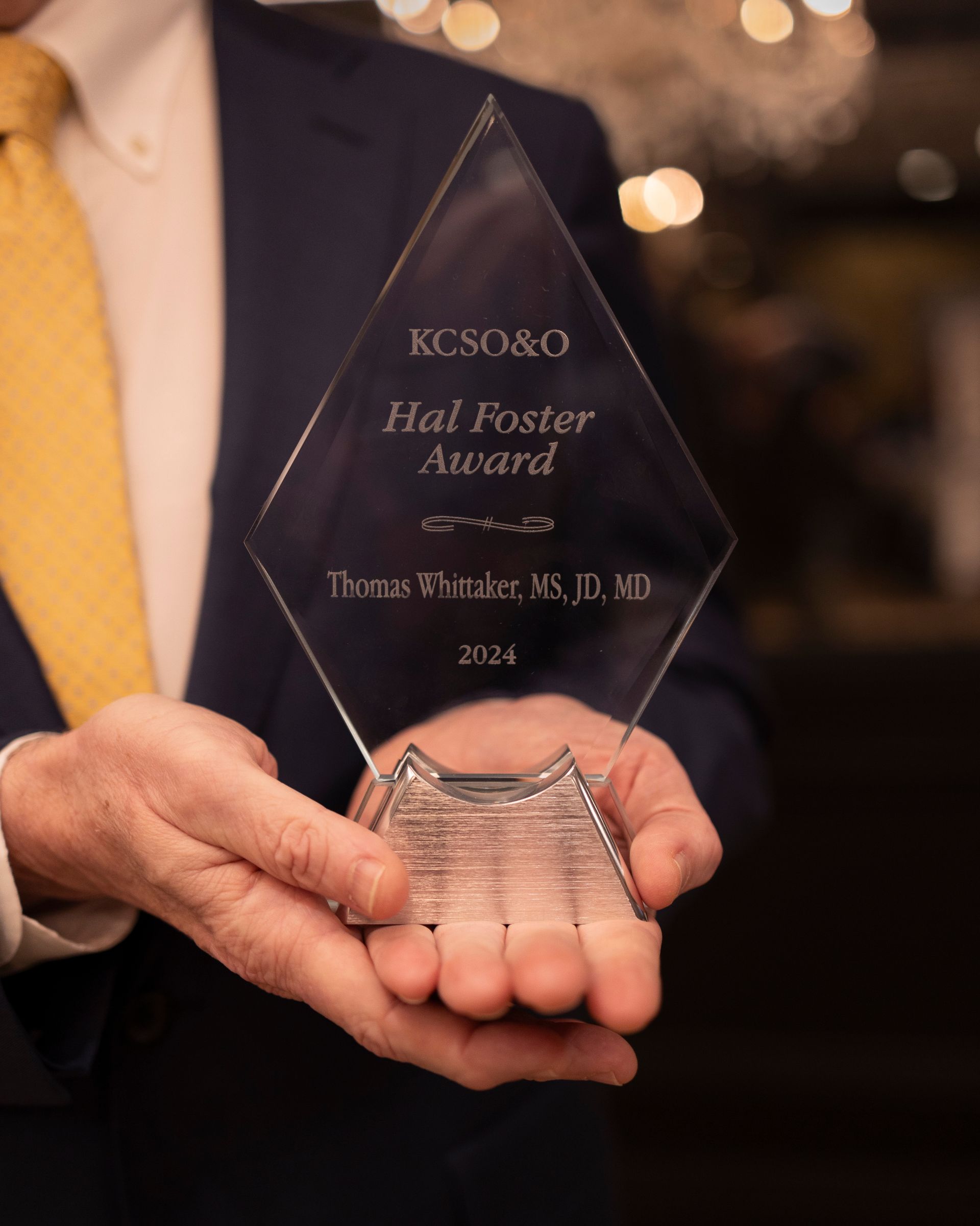 A man in a suit and tie is holding a trophy that says hal foster award