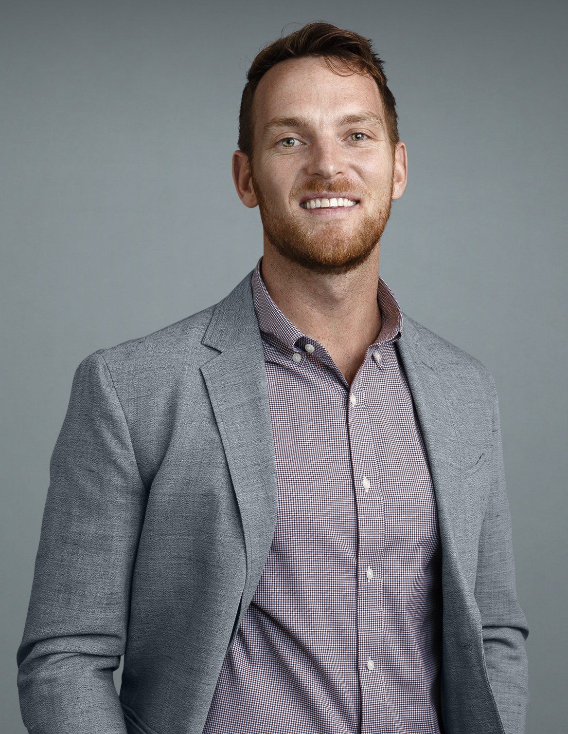 A man with a beard is wearing a suit jacket and a plaid shirt.