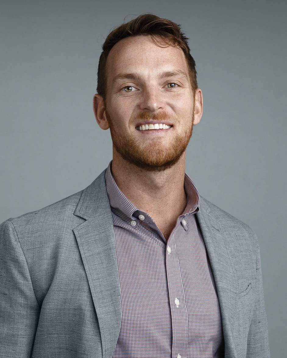 A man with a beard is wearing a suit jacket and a plaid shirt.