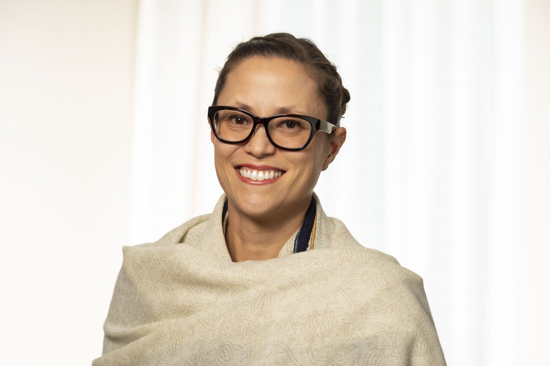 A woman wearing glasses and a shawl is smiling for the camera.