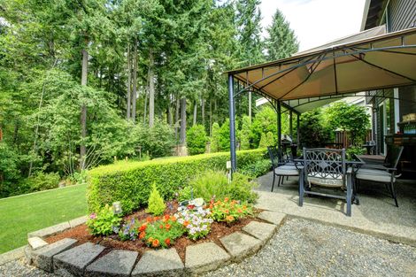 Patio con pergolato e mobili da esterno, delimitato da un'aiuola e da vegetazione.