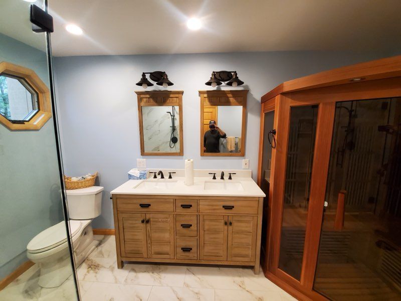 Bathroom with double vanity, mirrors, sauna, and toilet; light blue walls and wood accents.