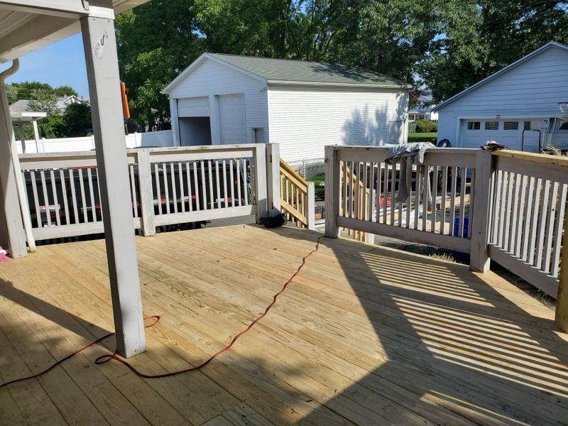 Wooden deck with gray railing, leads to stairs, buildings in background.