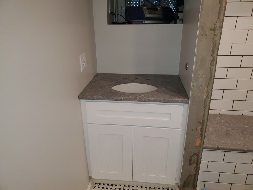 White bathroom vanity with gray countertop and sink, beneath a window.