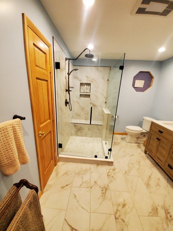 Modern bathroom with marble tile, glass shower, wooden vanity, and blue walls.