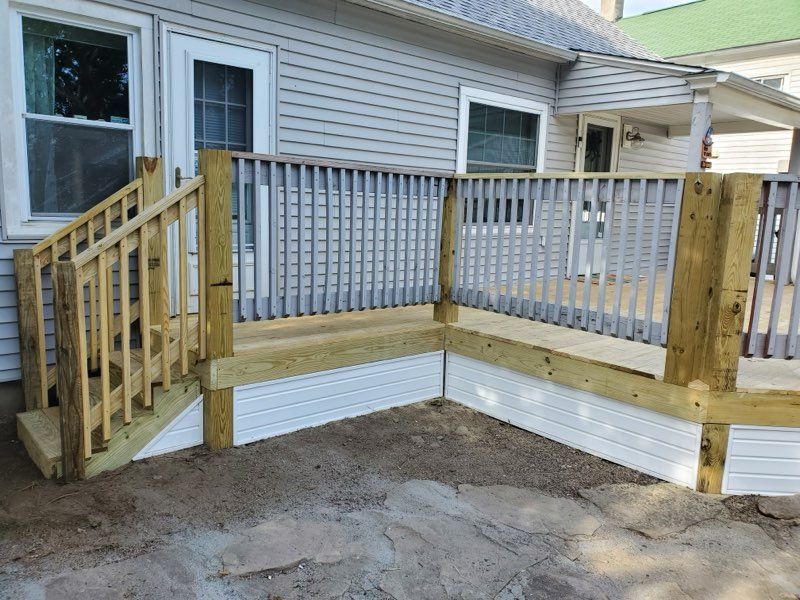 Newly constructed wooden deck with railings, stairs, and white skirting, next to a light gray house.