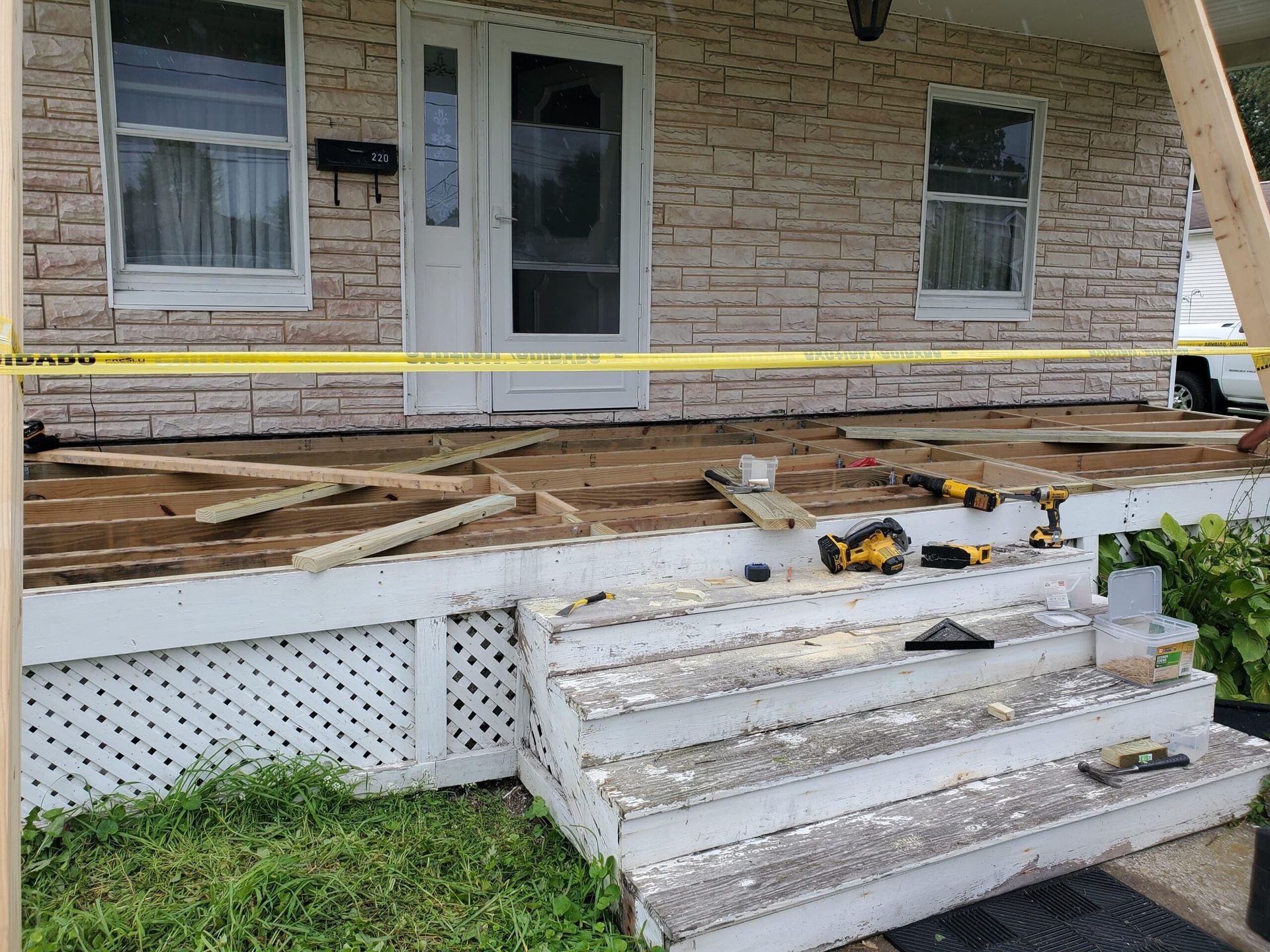 House porch under repair; wood deck boards removed, tools visible. Yellow caution tape.