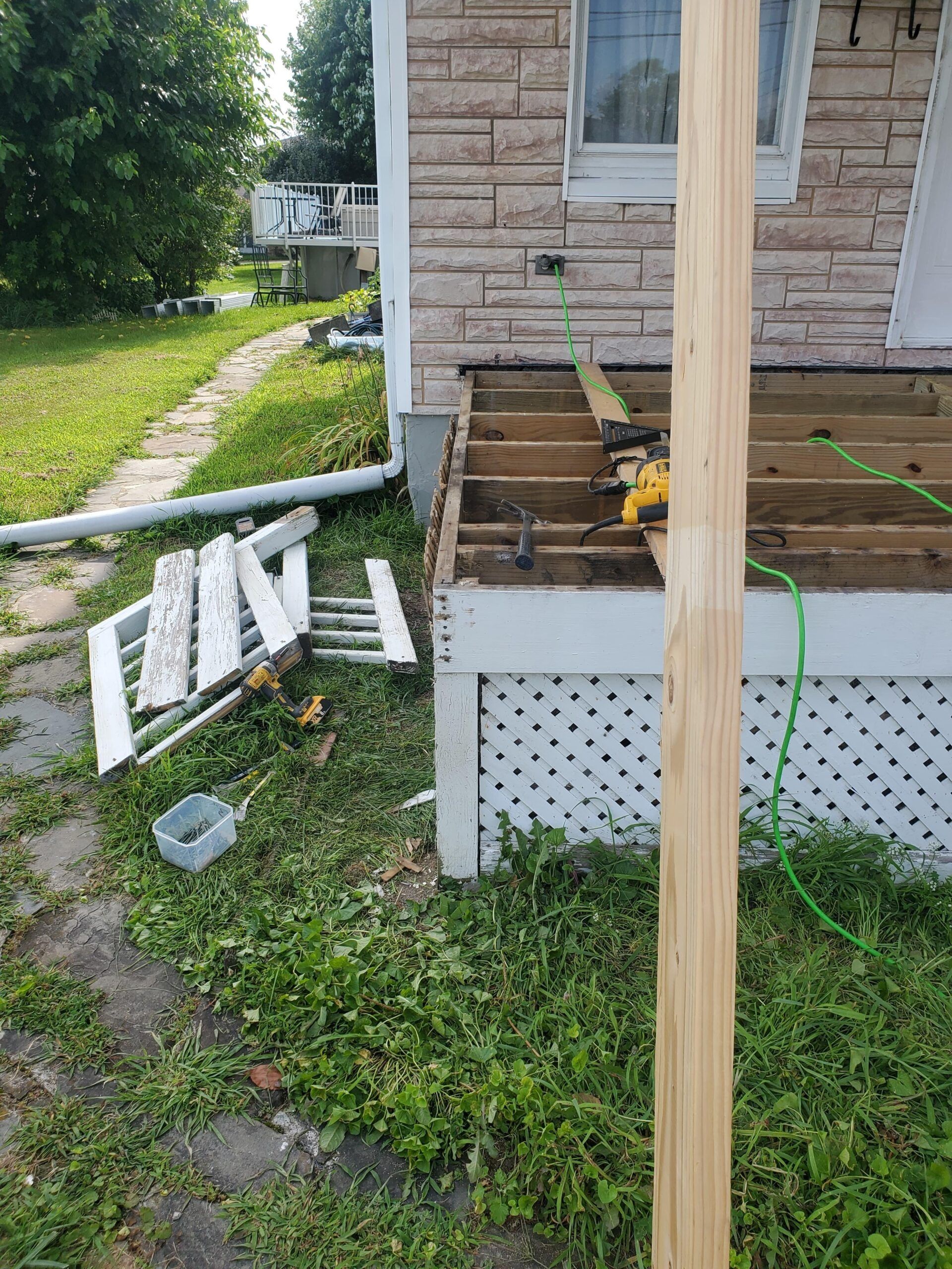 Porch deck under construction, tools and materials scattered. Building is light stone and white lattice.