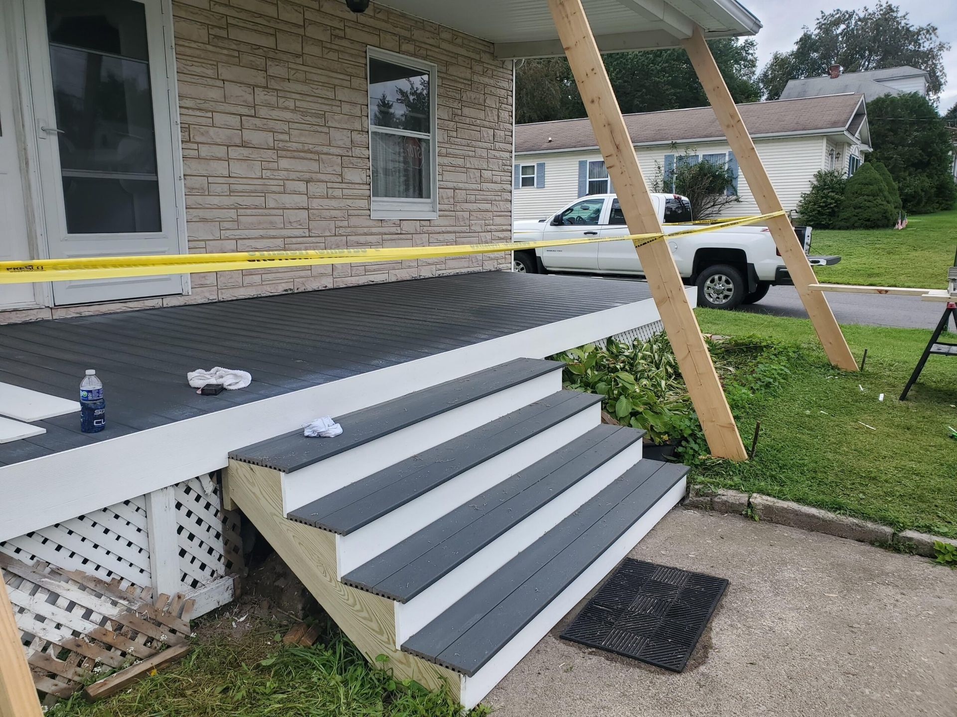 A house porch with yellow tape, steps, and support beams. A white truck is in the background.