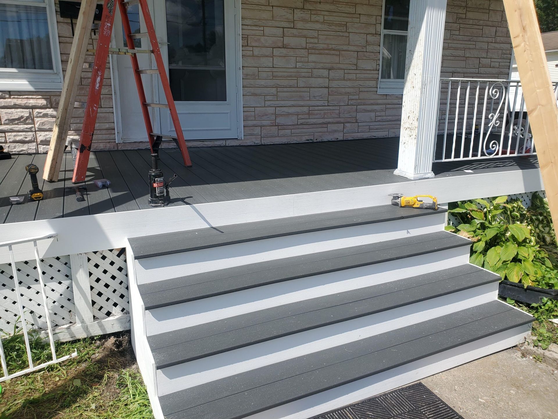 Renovated porch and stairs with gray composite decking and white trim, ladder propped up.