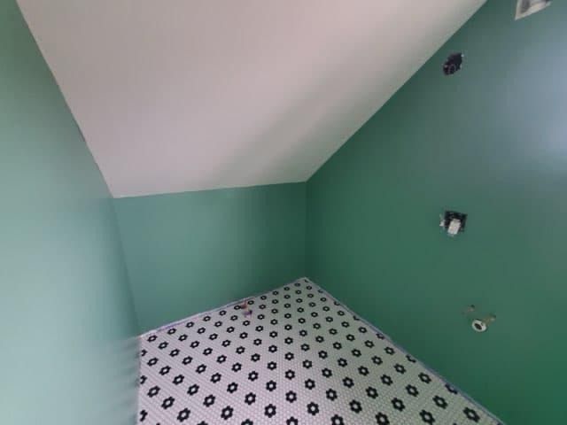 Green-walled room with sloped ceiling, patterned floor. White ceiling, three holes in wall, one light fixture.