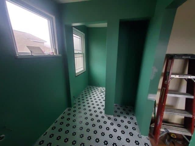 Green-painted room with black and white patterned tile floor, a window, and a red ladder.