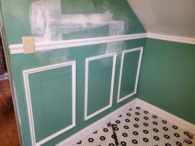 Green wall with white trim and rectangular frames; bathroom corner.