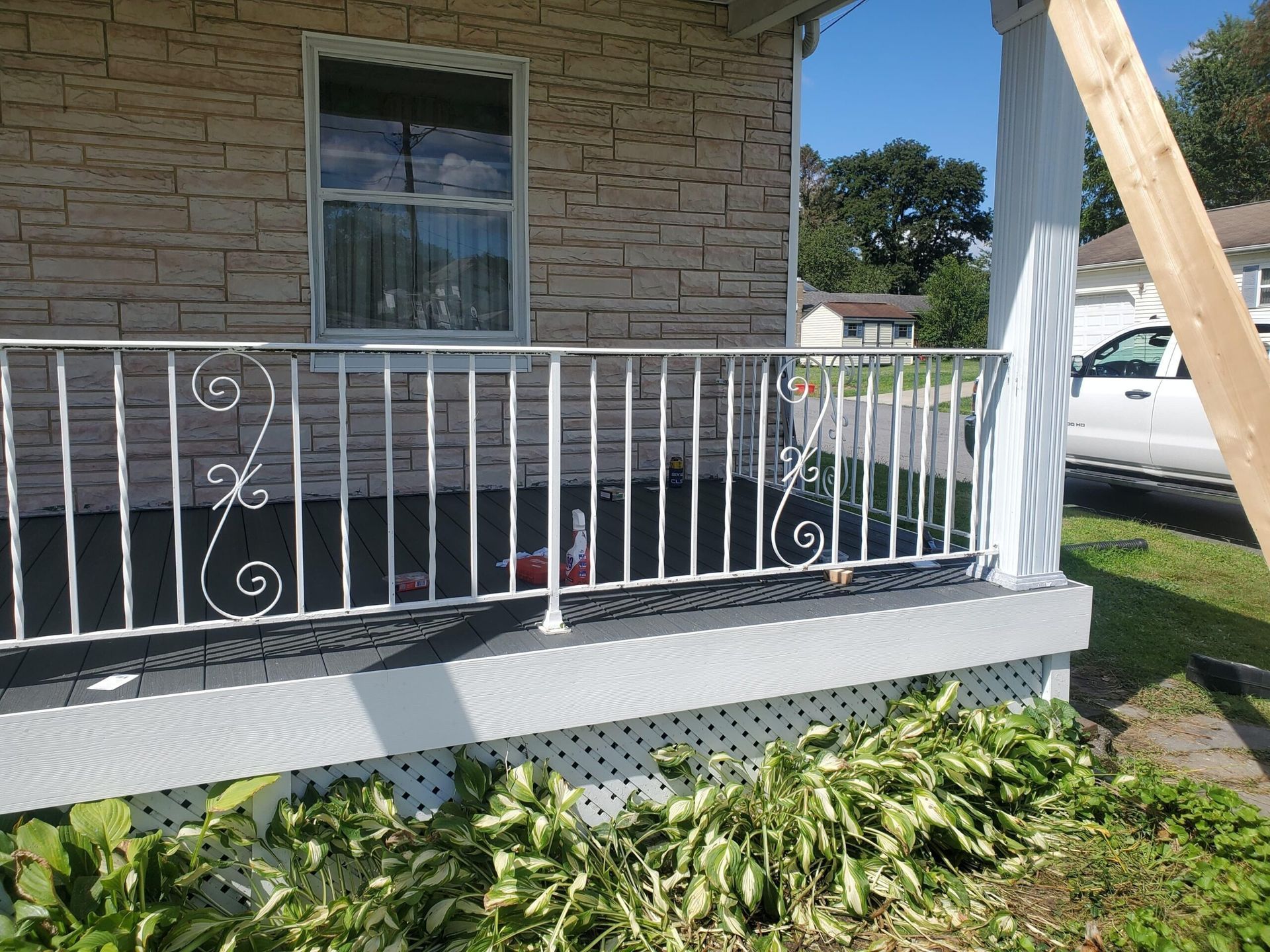 White porch railing with decorative swirls, in front of a house with a tan brick-like facade.