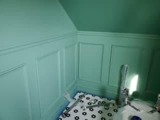 Green-painted bathroom walls with decorative panels, tile floor, and faucet fixtures.