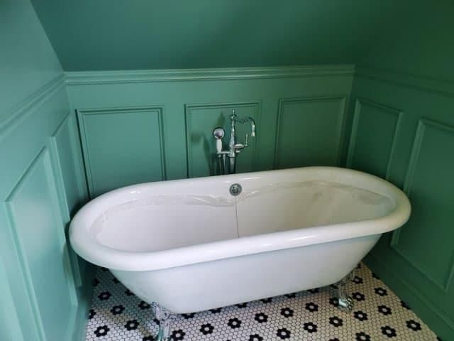 Oval white clawfoot bathtub against green paneling; black and white tiled floor.