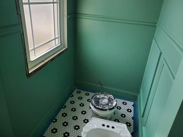 Small bathroom with green walls, mosaic tile floor, toilet, and window.
