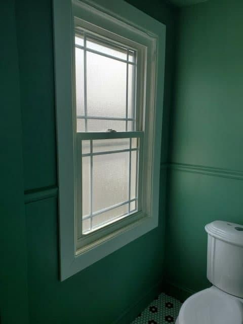 Green-walled bathroom with frosted window and white trim; toilet on the right.