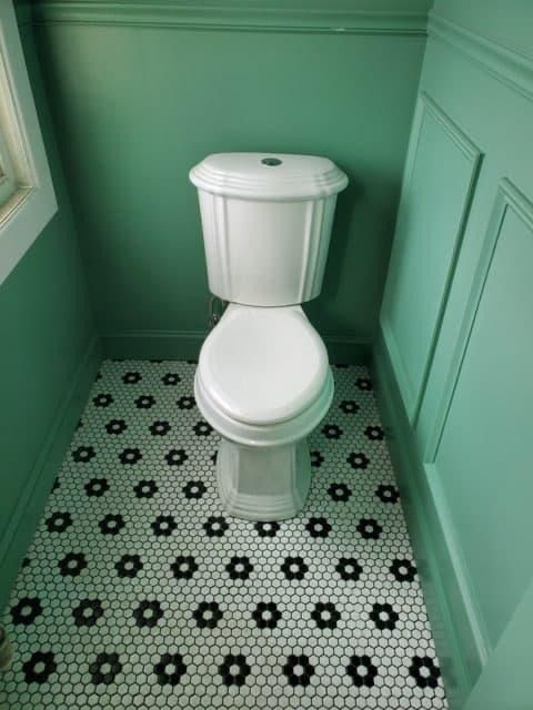 White toilet in a small room with green walls and black and white flower tile floor.