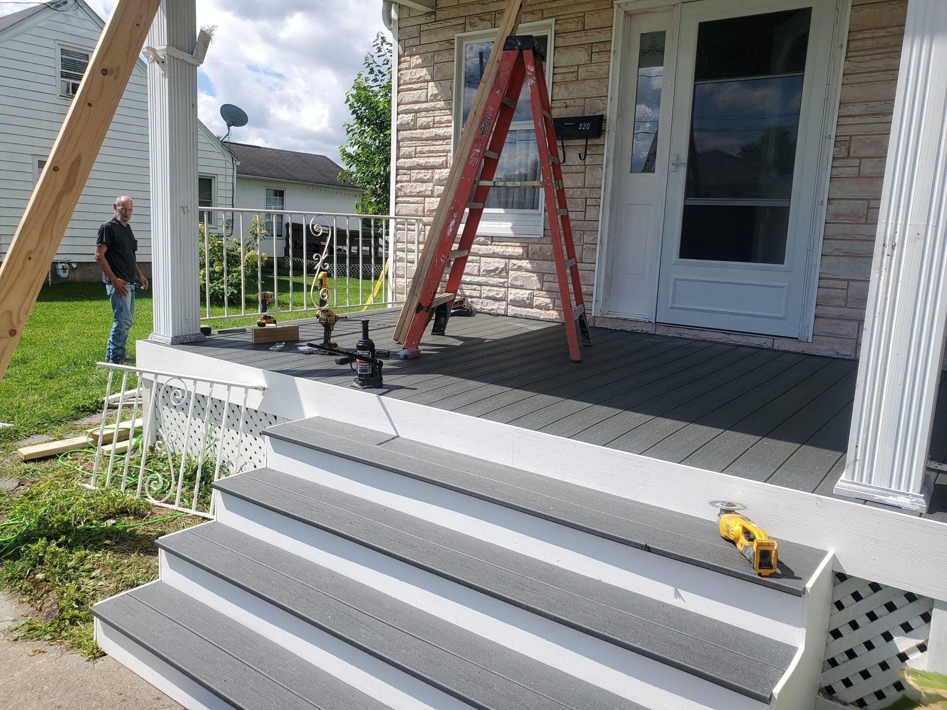 Porch with gray steps, ladder, and person on lawn, possibly under construction.