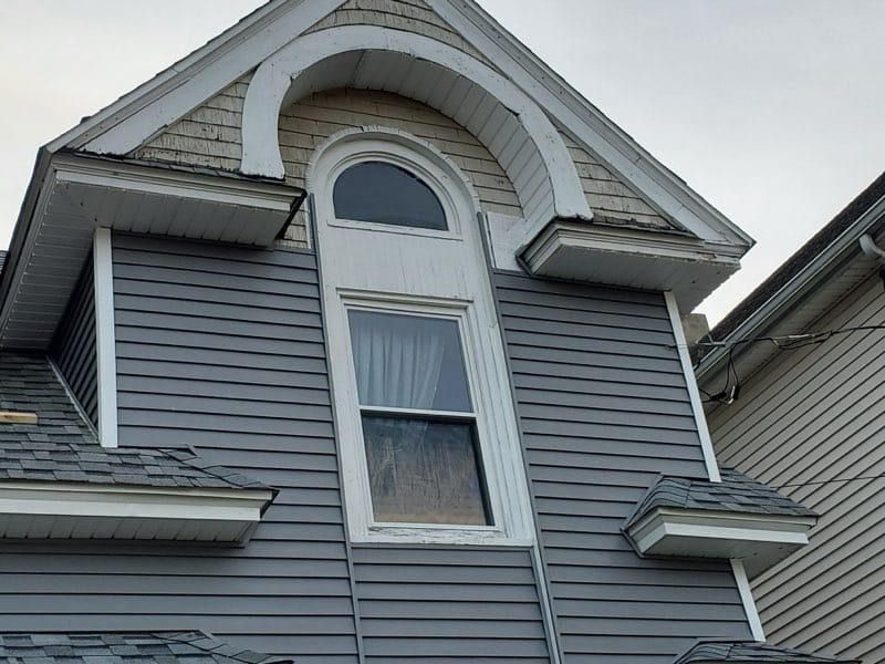 Gray house exterior with gabled roof, arched window above a rectangular window.