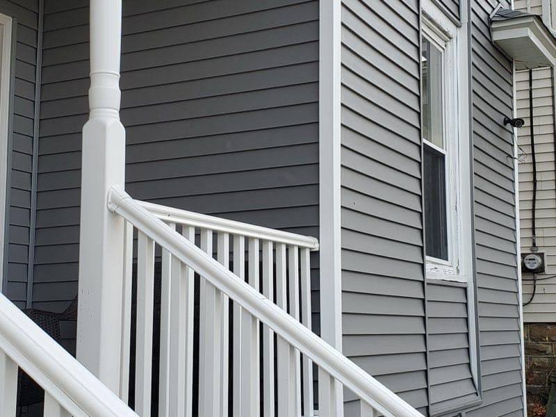 White porch railing and column, gray siding, window.