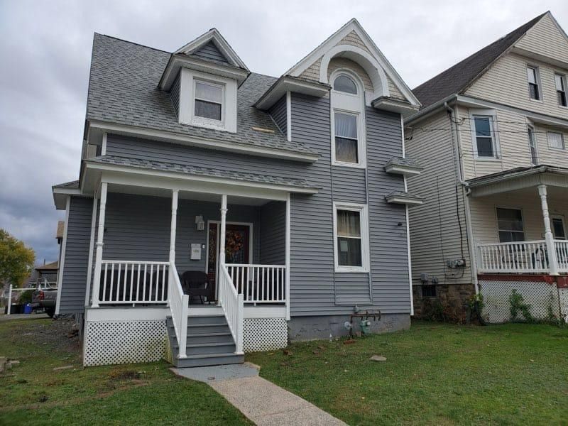 Gray two-story house with porch and dormers, next to a similar building.