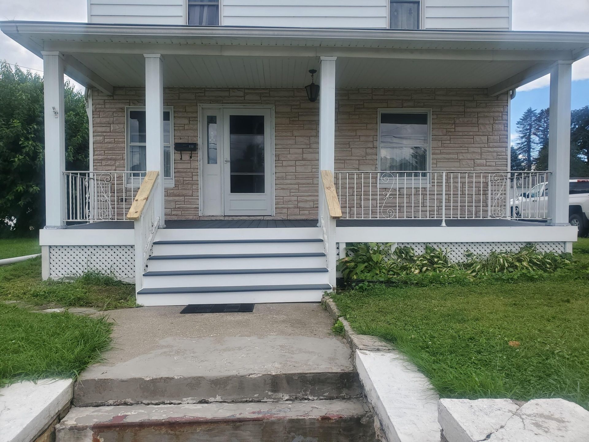 Stone house with porch and steps leading to the front door. White railings and porch posts.