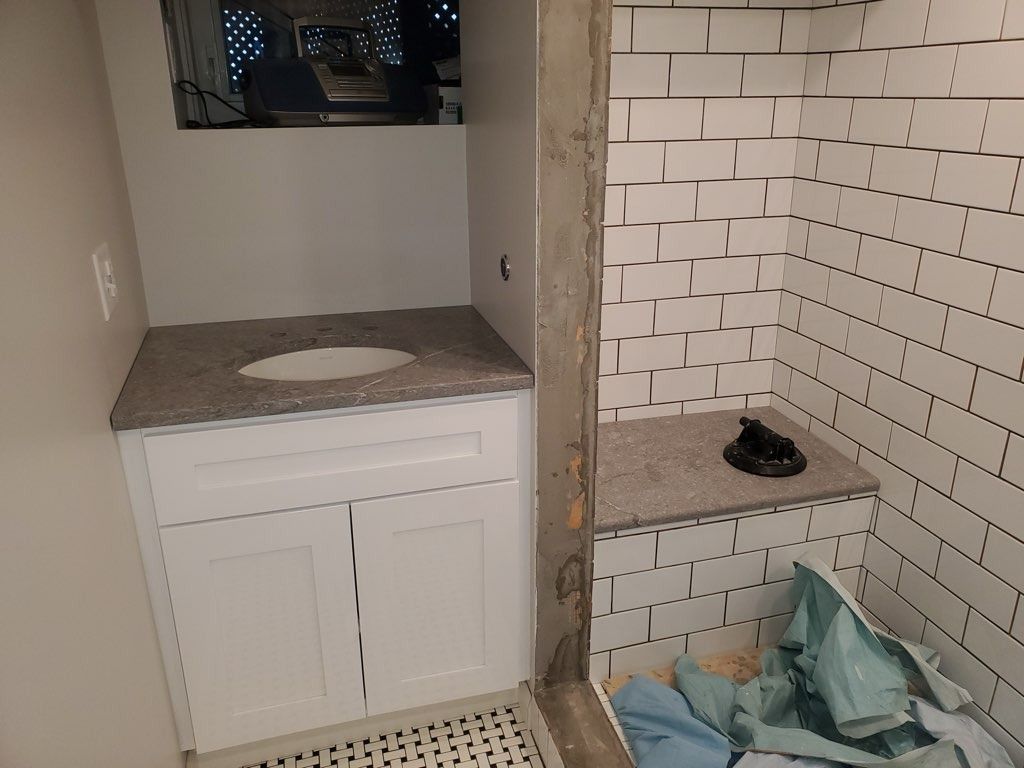 Bathroom renovation: white vanity with granite countertop, tiled shower, exposed concrete column, window above vanity.