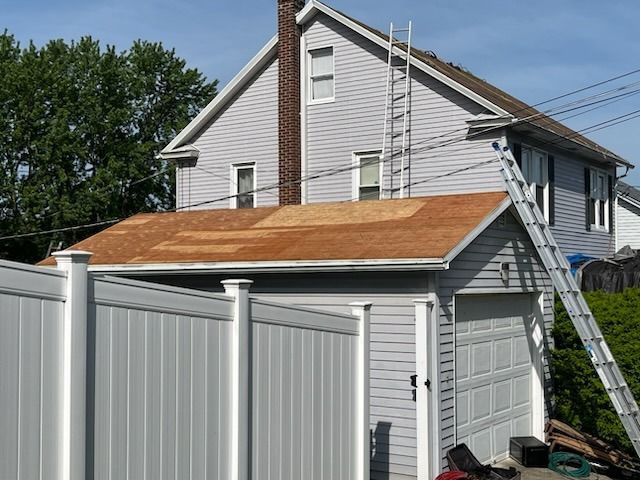Garage with exposed roof being worked on, ladder leaning against the structure. White fence in foreground.