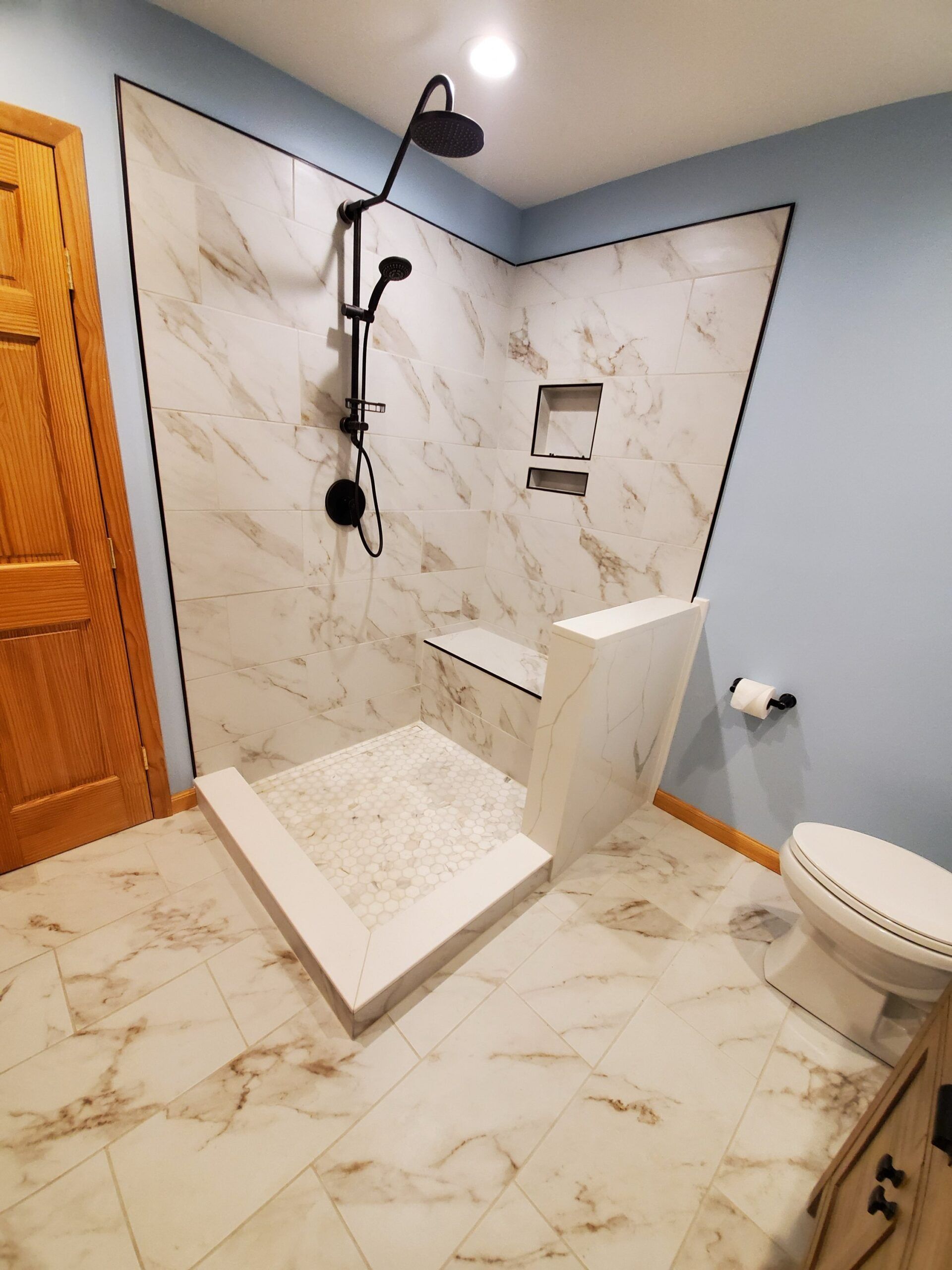 Modern shower with white marble tiles and black fixtures.