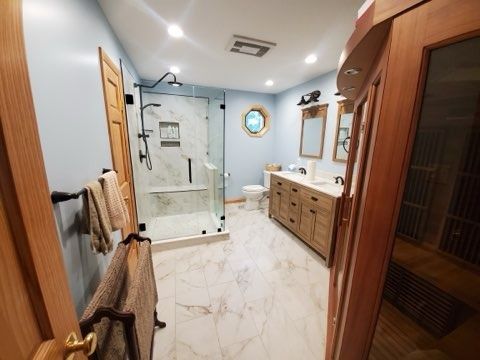 Spacious bathroom with glass shower, light blue walls, wood vanity, and tile floor.