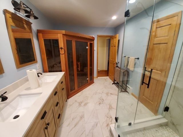 Bathroom with wooden cabinetry, marble floors, glass shower, and sauna.