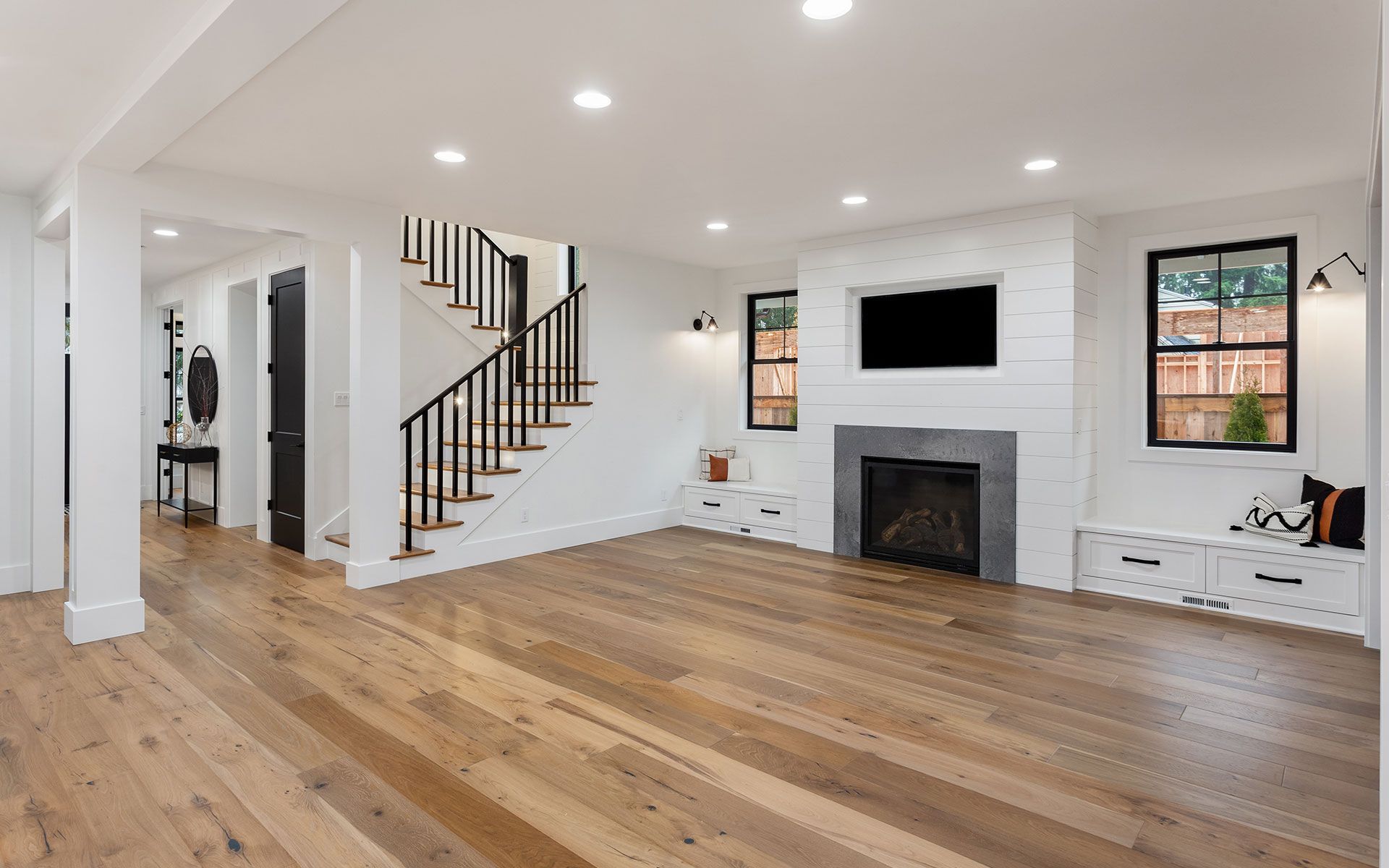 Empty living room with wood floors, white walls, fireplace, and staircase.