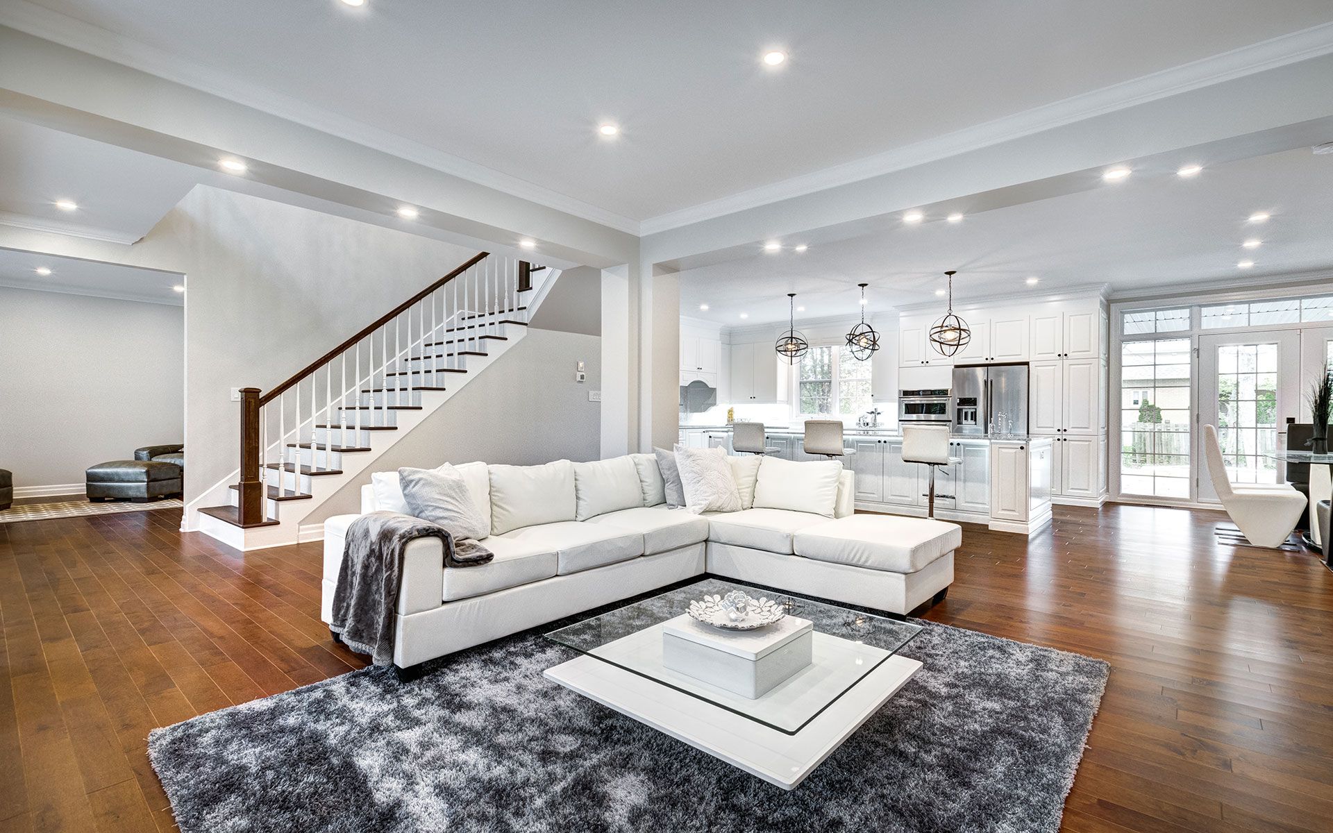 Living room with white sectional sofa, stairs, and open kitchen.