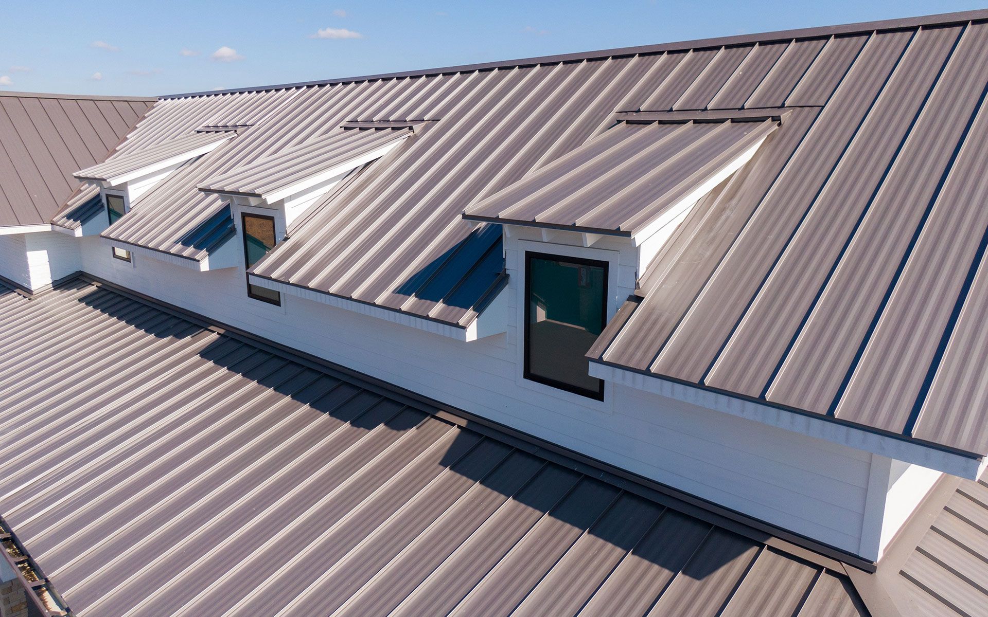 Gray metal roof with three white dormers with windows.
