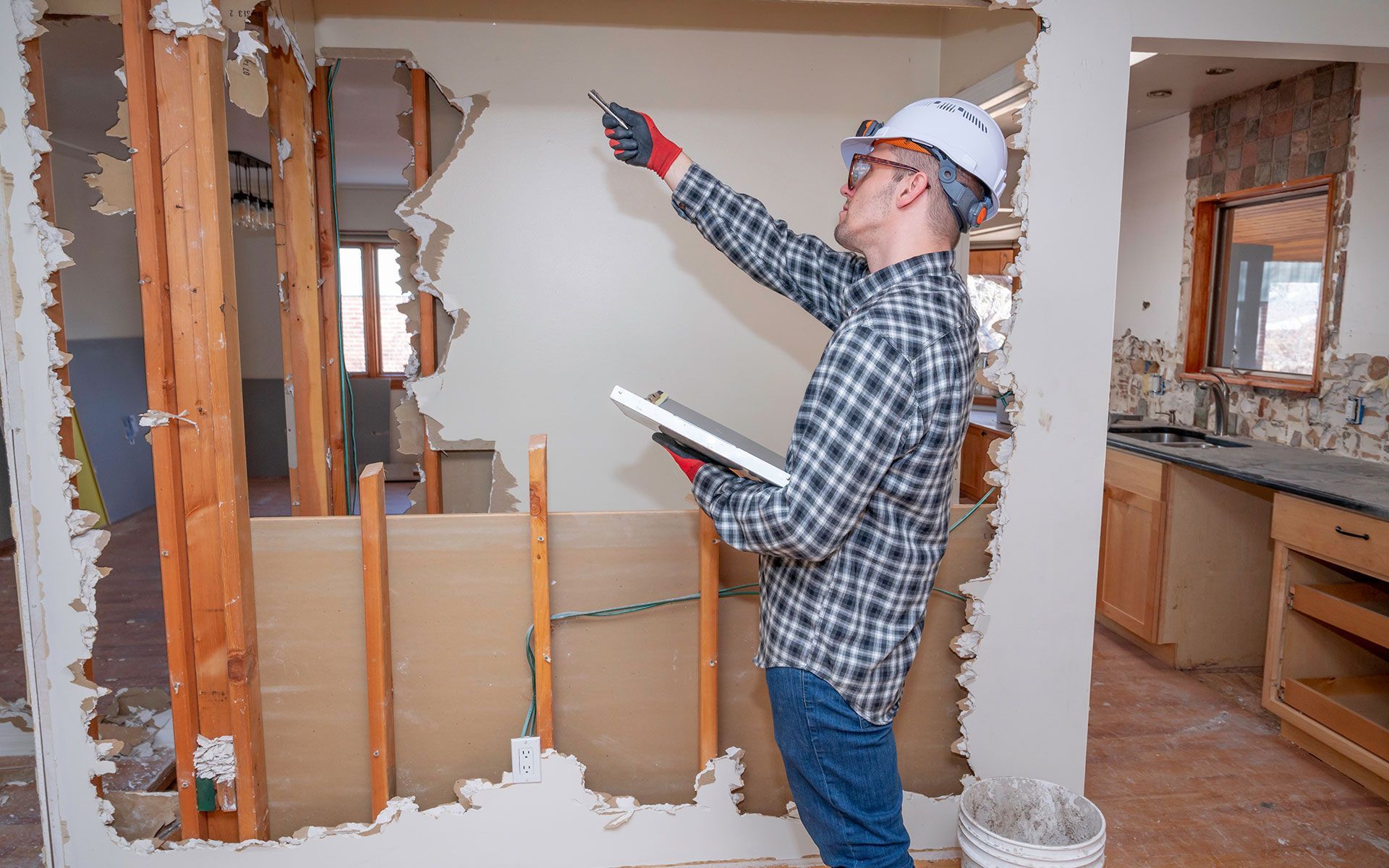 Construction worker inspecting damaged wall with a tablet.