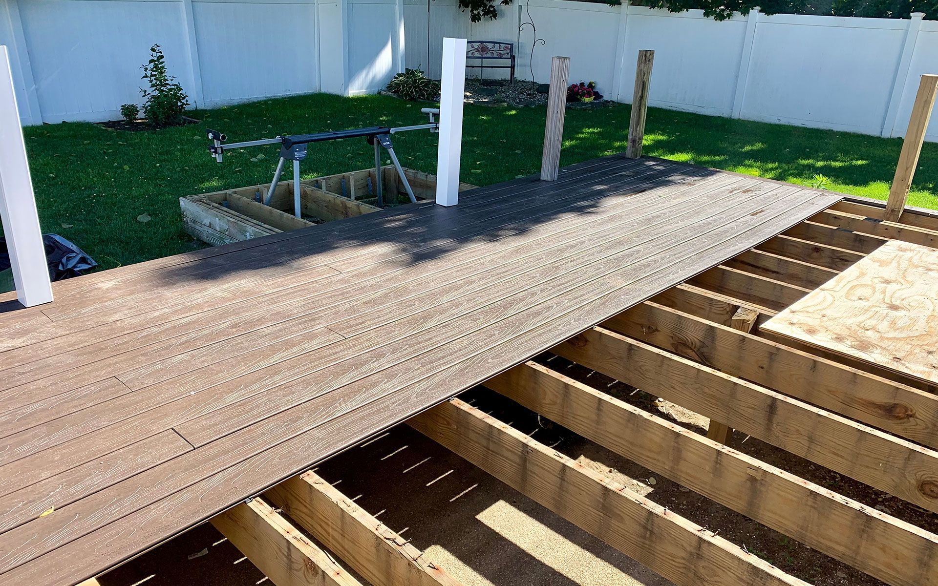 Construction of a wooden deck; close-up of a partially completed deck with brown composite decking laid over wooden joists.