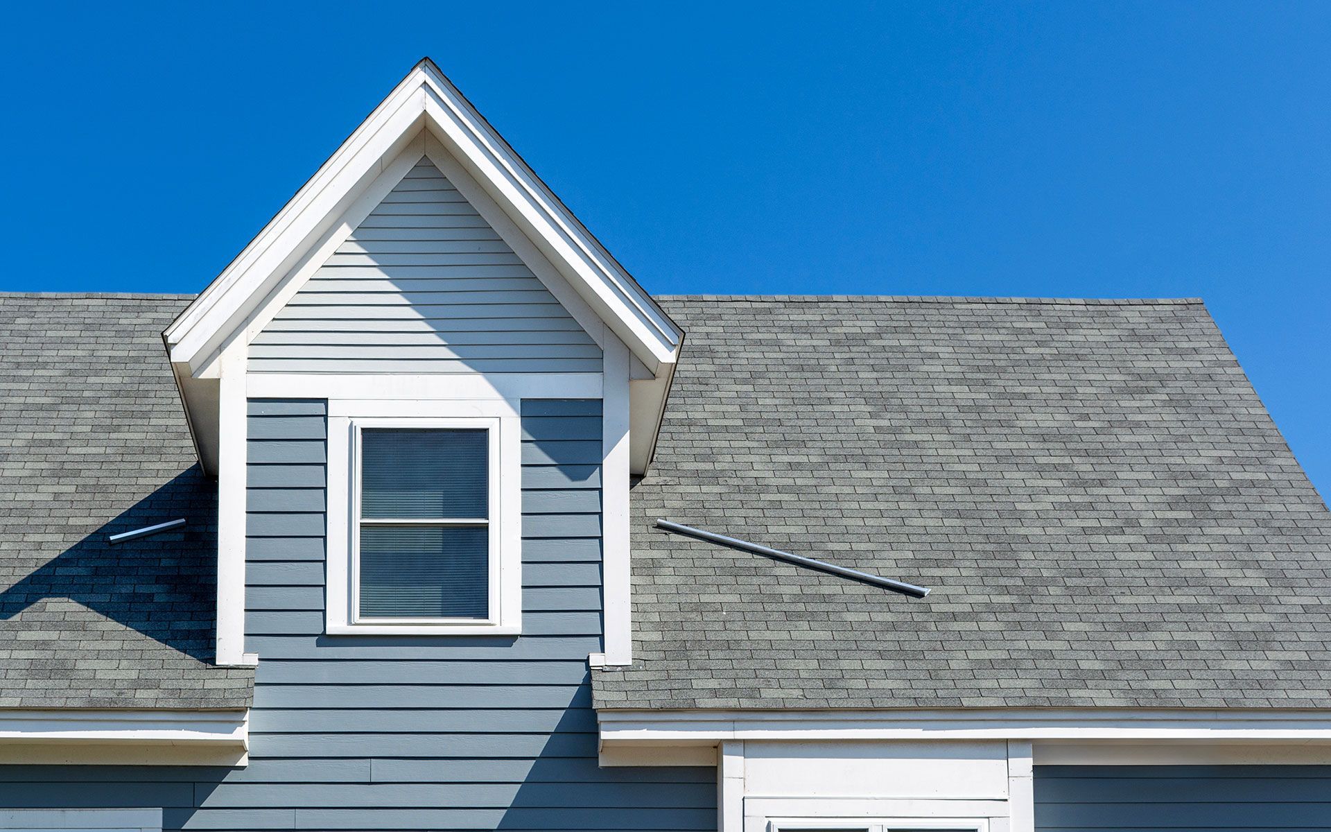 Blue house with a gray roof and a white-trimmed window against a clear blue sky.