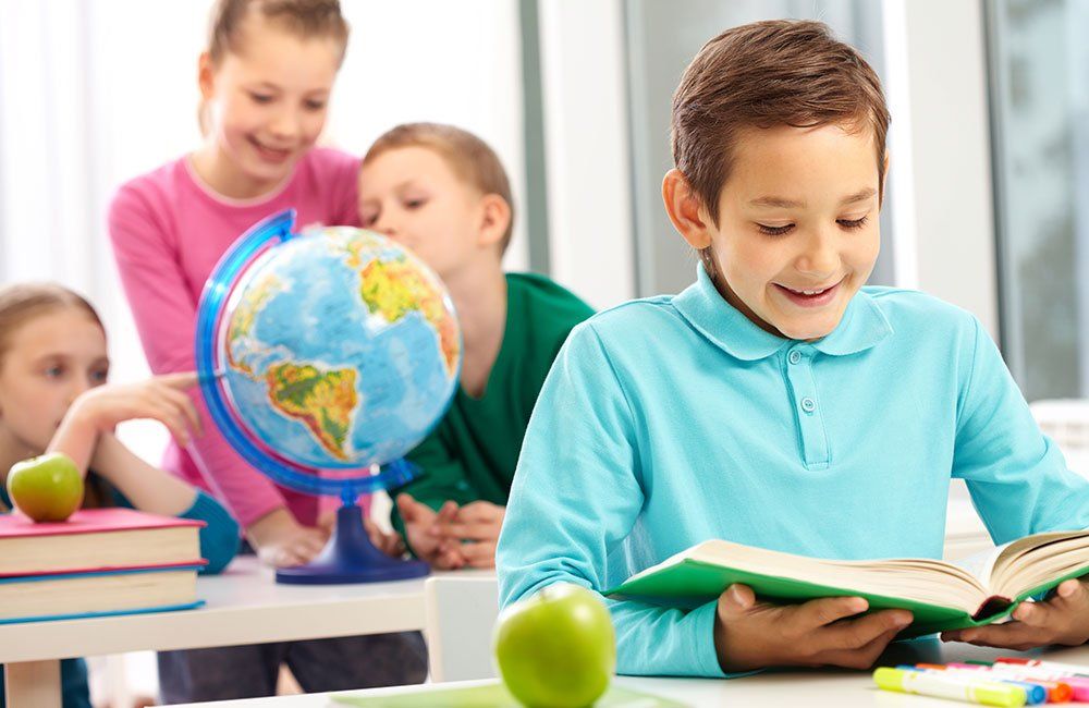 A boy is reading a book in a classroom with a globe in the background.