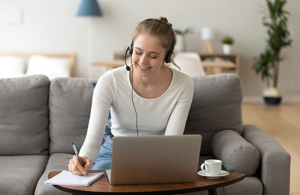 A woman wearing headphones is sitting on a couch using a laptop computer.