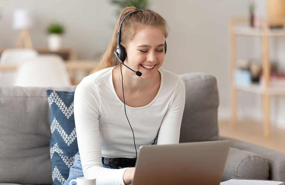A woman wearing headphones is sitting on a couch using a laptop computer.