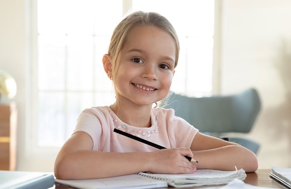 A little girl is sitting at a table writing in a notebook.
