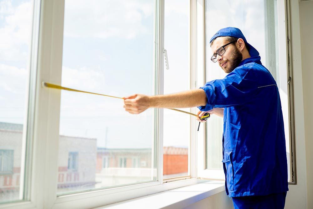 A man dressed in blue uniform stands with a stick, supervising residential window replacement in Cin