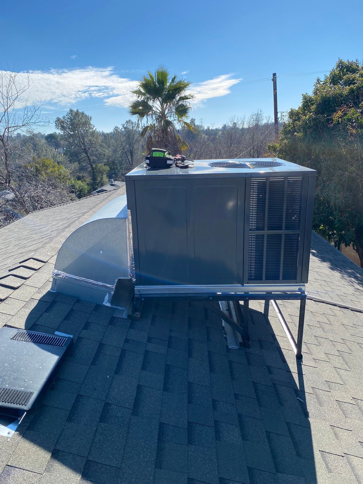 Roof-mounted HVAC unit on a sloped rooftop under a bright blue sky, with trees in the background