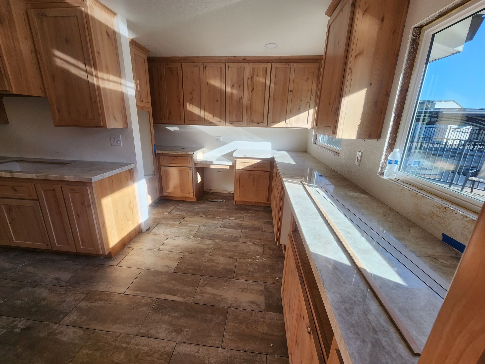 Empty unfinished kitchen with wood cabinets, worn floor, and sunlight through a window